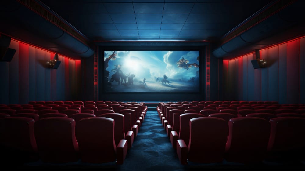 Empty cinema with red upholstered seats facing a large screen showing a bright dinosaur-filled scene.