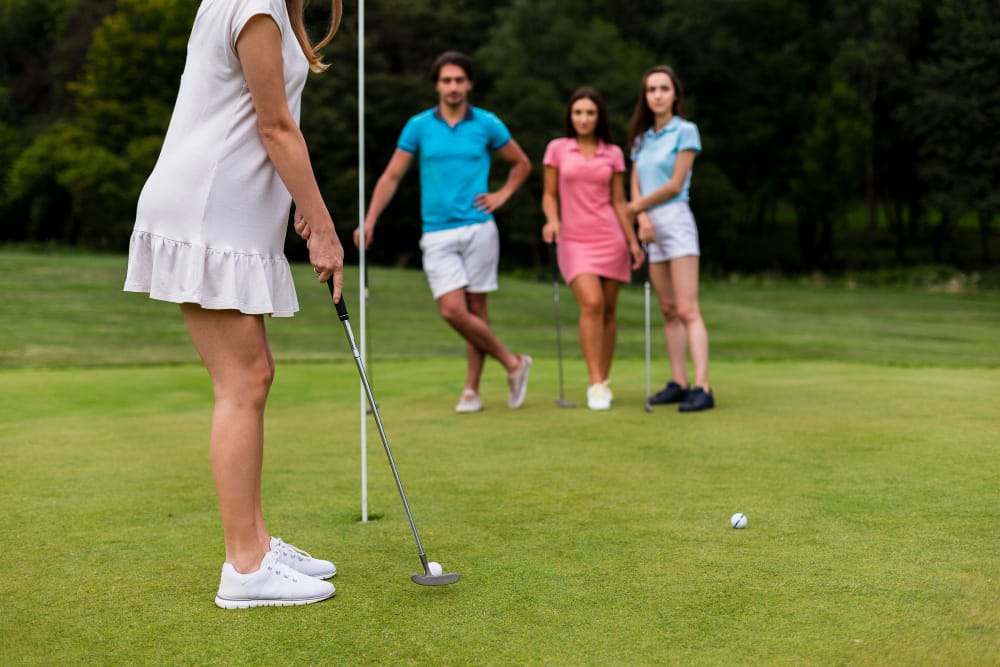 Woman in a white dress lines up a putt on a greens with a flagstick nearby as three friends watch in the background.