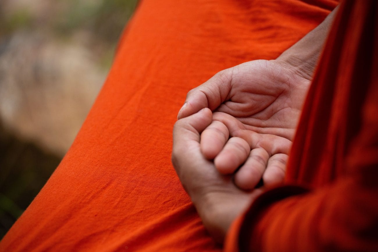Close-up of cupped hands resting on bright orange fabric, suggesting meditation or prayer.