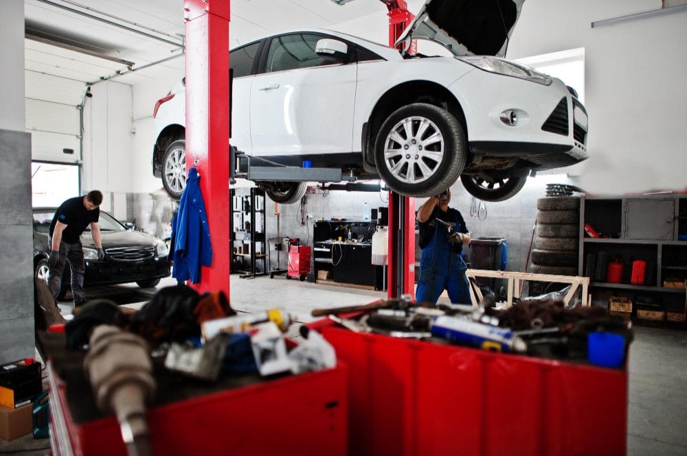 778548 - Taller J Álvarez - Hunter Magazine White car raised on a hydraulic lift in a busy auto repair shop with technicians working nearby